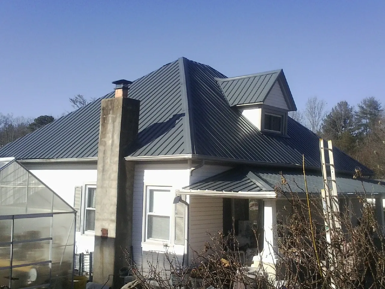 Dark blue standing seam metal roof on a white farmhouse with dormer — Slate & Tile Roof Repair by Roofing Brothers in Purcell