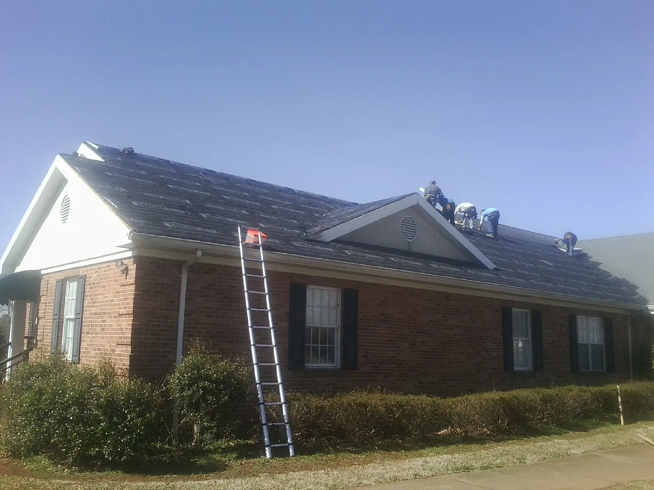 Crew tearing shingles off a brick ranch roof with a ladder set — Emergency Roof Repair work by our crew in Purcell