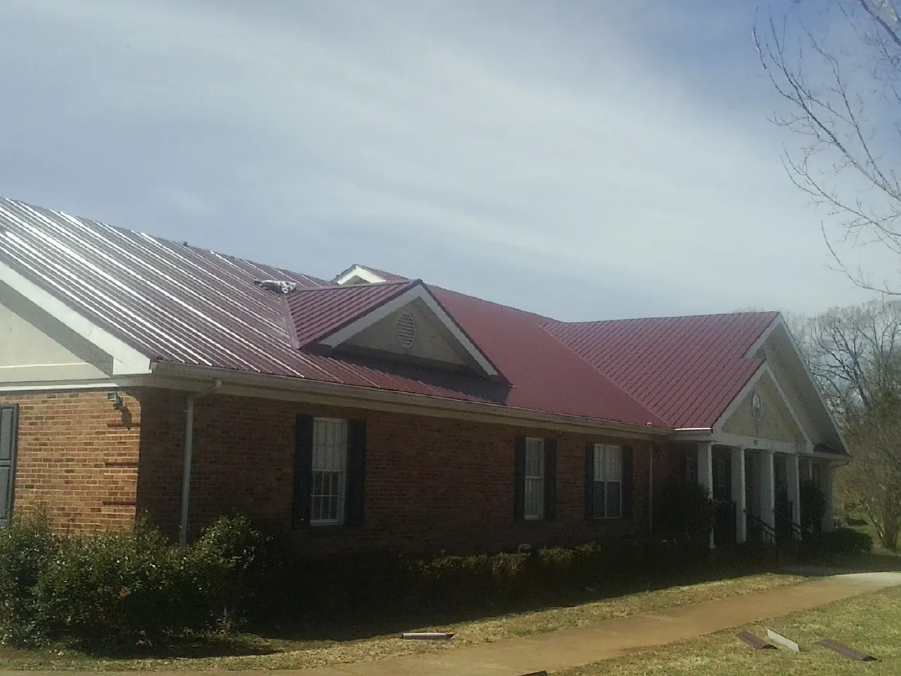 Red metal roof with gabled entries on a long brick building, from a Hail Damage Roof Repair job in Purcell