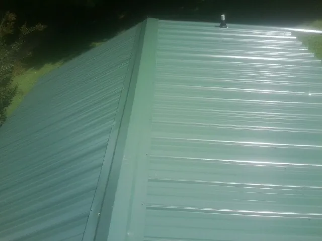 New green metal panels meeting at the ridge of a roof — Flat Roof Repair work by our crew in Purcell