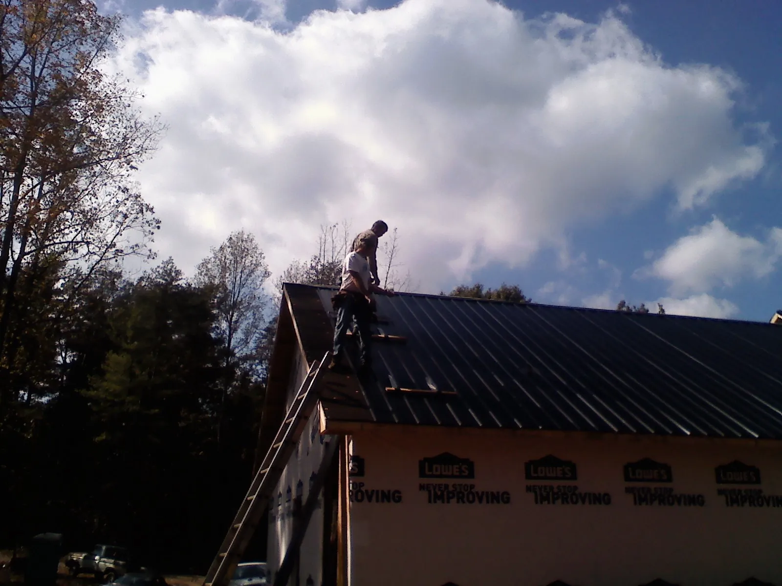 Roofer fastening dark metal panels high against a cloudy sky, from a Roof Inspection job in Purcell