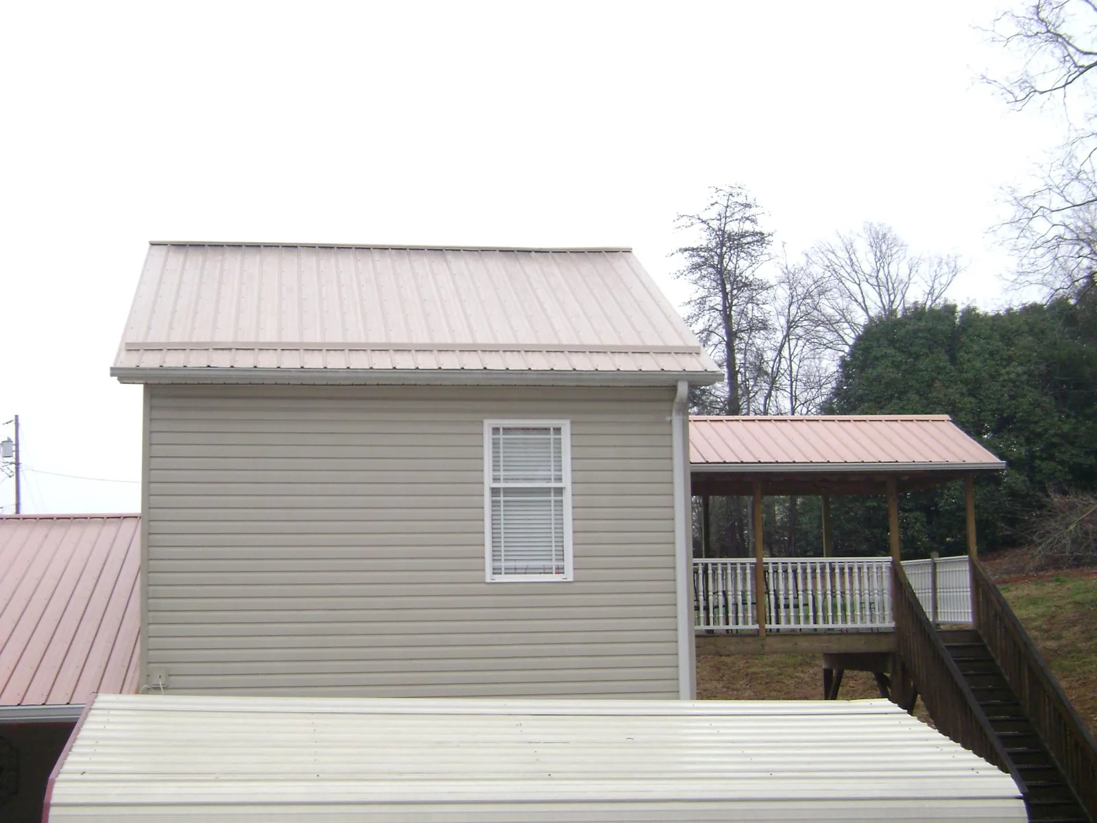 Tan metal roofs on a two story addition and attached porch, from a Roof Replacement job in Purcell